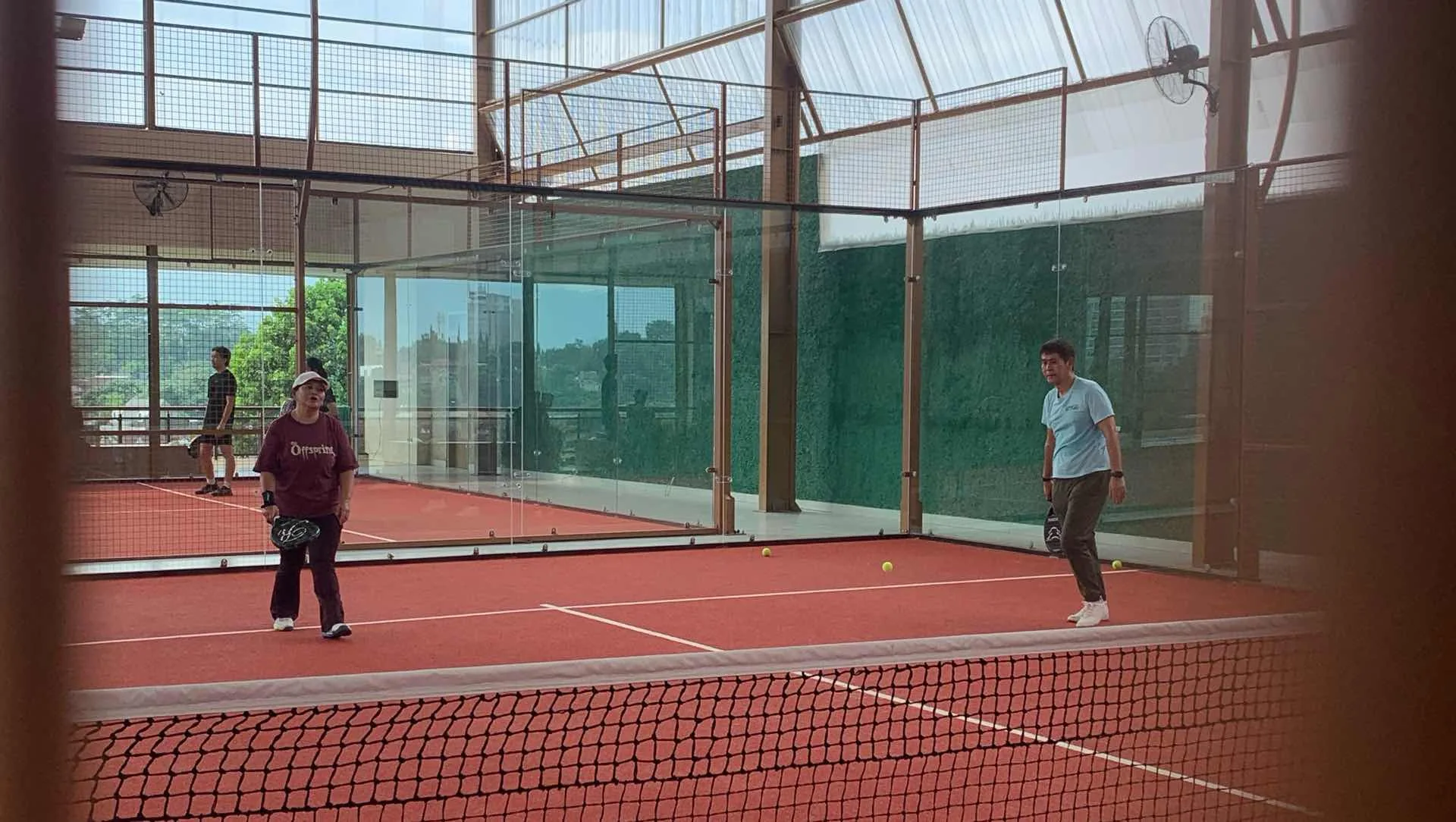 Two players in a rally, seen through the glass of a PCC Bogor court